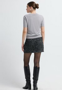 Lys grå kort�ærmet striktop parret med en knælang sort kjole med paljetter. Sorte knæhøje læderstøvler komplimenterer outfittet.