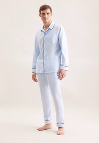 Ensemble de pyjama bleu clair en tissu doux. Chemise boutonnée avec une poche et un liseré noir, associée à un pantalon assorti avec des ourlets côtelés.
