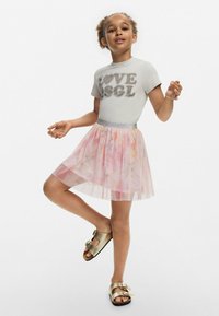 Szürke póló, amelyen a "LOVE" felirat strasszokkal van nyomtatva, világos rózsaszín tüll szoknyával párosítva, virágmintákkal és ezüst övvel, valamint arany szandálokkal.