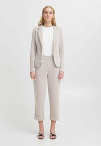 Ljusgrå skräddarsydd kavaj och matchande croppade byxor, tillverkade av mjukt tyg, med uppvikt ärm och en vit topp under. Svarta sandaler.