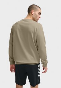 Ljusbeige sweatshirt med långa ärmar, rund halsringning, jämn textur, kombinerad med svarta shorts med vita chevron-accenter.