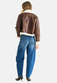 Brown leather cropped jacket with fur collar and cuffs, paired with loose blue jeans and heeled ankle boots, viewed from the back.