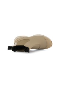 Zapato sin cordones beige con parte superior de cuero, punta redonda y detalles elásticos negros. Suela plana con agarre texturizado que mejora la estabilidad.