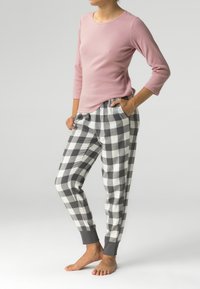 Jasnoróżowa bluzka z długim rękawem o teksturze prążkowanej, zestawiona z szaro-białymi piżamowymi spodniami w kratkę, wyposażonymi w elastyczny pas i mankiety.