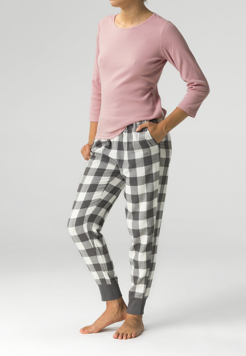 Jasnoróżowa bluzka z długim rękawem o teksturze prążkowanej, zestawiona z szaro-białymi piżamowymi spodniami w kratkę, wyposażonymi w elastyczny pas i mankiety.