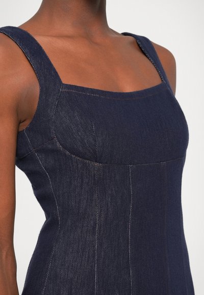 Tmavomodré džinsové šaty so štvorcovým výstrihom, širokými ramienkami a priliehavým strihom. Obsahujú viditeľné švy a štruktúrovanú tkaninu pre zvýraznenie detailov.