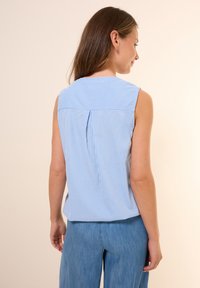 Haut sans manches rayé bleu et blanc avec un col haut, présentant un détail de pli au dos. Associé à un pantalon en denim clair à jambes larges.