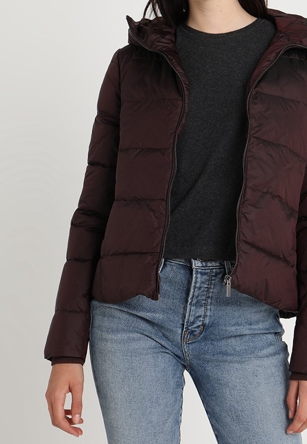 Doudoune bordeaux avec fermeture éclair à l'avant et capuche, présentant un motif matelassé et des poignets élastiques. Port ée sur un haut foncé et un jean bleu clair.