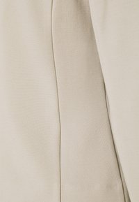 Beige Stoff mit einer glatten Textur, der einen subtilen Glanz aufweist. Nahtdetails erzeugen ein strukturiertes Design. Weiches und leichtes Material.