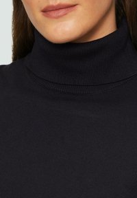 Zwarte coltrui met een geribbelde textuur en hoge kraag, met close-up detail van de nek en het bovenste deel van de borst.