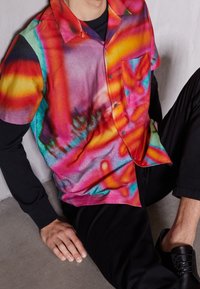 Chemise à manches courtes avec un motif tie-dye vibrant en nuances de rose, orange et bleu, dotée d'une patte de boutonnage et d'une poche poitrine.