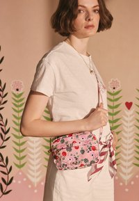Lyserød blomster crossbody taske med sorte detaljer, rektangulær form, justerbar rem, quiltet tekstur og guldelementer.