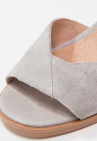 Sandalo in suede grigio con design a fascetta incrociata, suola piatta e soletta beige. Presenta dettagli cuciti e una texture liscia.