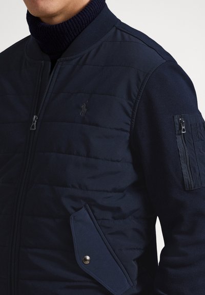 Μπουφάν ναυτικού τύπου με ριμπ γιακά, τσέπη στο μανίκι με φερμουάρ και λεπτομέρεια με κουμπιά στο μπροστινό τσεπάκι· κομψός σχεδιασμός και υφή υφάσματος.