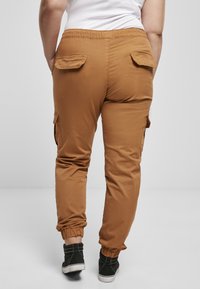 Pruuni cargo-püksid elastse vöökoha, küljetaskute ja korjatud sääreotstega. Kanga pind on sile ja matt.