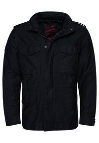 Zwarte veldjas gemaakt van katoen met een ritssluiting en drukknoopsluiting, voorzien van vier voorzakken en een opstaande kraag.