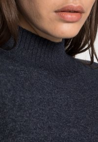 Mörkblå polotröja med ribbad struktur, slät tygkvalitet och figursydd design. Närbild av halsringning och övre tygdetaljer.