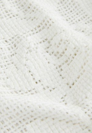 Balts teksturēts audums ar brīvi austiem rakstiem un režģa formas atverēm, izceļot mīkstumu un dziļumu.