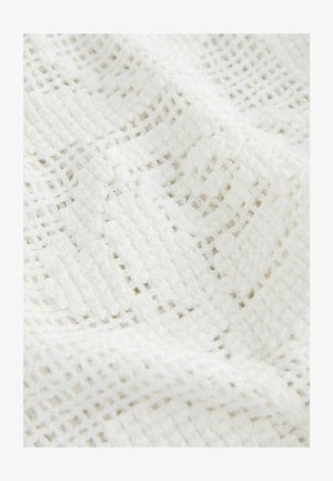 Balts teksturēts audums ar brīvi austiem rakstiem un režģa formas atverēm, izceļot mīkstumu un dziļumu.