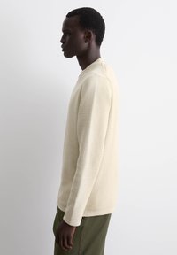 Helles beige gestricktes Sweatshirt mit Rundhalsausschnitt, langen Ärmeln und gerippten Bündchen. Es hat einen strukturierten Stoff und eine lockere Passform.