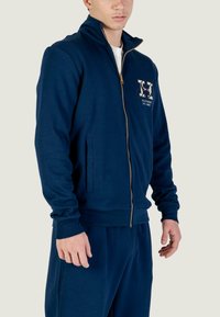 Felpa blu navy con zip in misto cotone, colletto alto, zip dorata, tasche laterali e dettaglio logo sul petto.