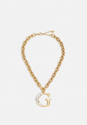 Collier en chaîne dorée avec un grand pendentif en forme de "G" orné de sept pierres précieuses claires sur un fond blanc.