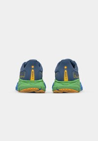 Baskets de course avec un design bleu, vert et jaune. Présentent une semelle texturée et un talon rembourré pour le soutien. Logo "ARAHI 7" visible.