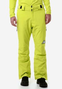 Pantaloni da sci giallo brillante con una texture liscia, dotati di una cintura nera e dettagli neri, tasche laterali e un logo sulla coscia sinistra.