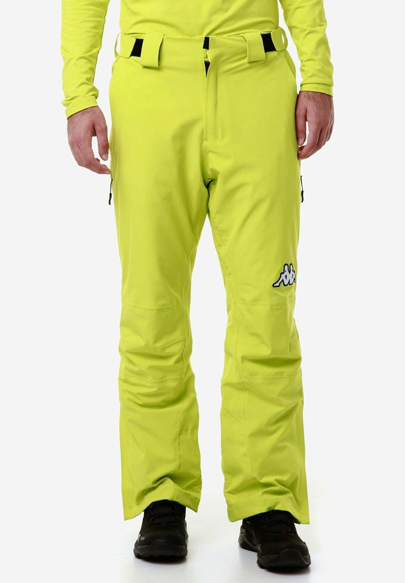 Pantaloni da sci giallo brillante con una texture liscia, dotati di una cintura nera e dettagli neri, tasche laterali e un logo sulla coscia sinistra.