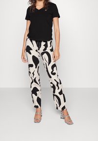 Czarna koszulka z dekoltem w serek w połączeniu z wysokim stanem w kolorze kremowym, ozdobionym odważnymi, czarnymi abstrakcyjnymi wzorami oraz w kratkę wysokimi sandałami na obcasie.