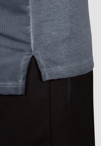 Camiseta gris con dobladillo redondeado, que presenta una tela texturizada y aberturas laterales. Combinada con pantalones negros, que muestran una textura suave y una cinturilla elástica.