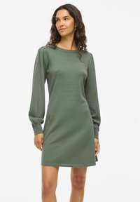 Abito a maniche lunghe di colore verde scuro, realizzato in tessuto morbido. Presenta un collo rotondo e dettagli arricciati sulle spalle per una vestibilità rilassata.