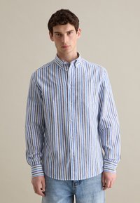 Camicia button-up a righe blu e bianche con colletto, maniche lunghe e taschino sul petto. Il tessuto sembra leggero e di una texture particolare.