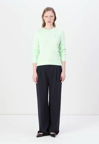 Un pull côtelé vert menthe à manches longues, associé à un pantalon navy ample et des chaussures plates noires. Design simple et texture légère.