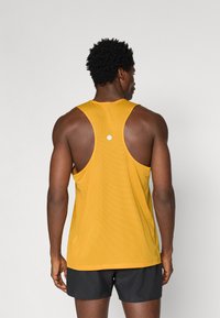 Κίτρινο ριπτό μπλουζάκι χωρίς μανίκια με στρογγυλή λαιμόκοψη και σχεδίαση racerback, featuring ένα μικρό λευκό λογότυπο στην πλάτη, φορεμένο με μαύρες σορτς.