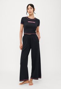 Černý crop top s růžovými detaily a nápisem "Lucid Dreams", doplněný volnými černými kalhotami s růžovými lemy. Měkká tkanina, volný střih.