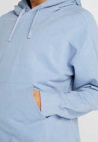 Sudadera azul claro hecha de tela suave, con un bolsillo delantero, capucha ajustable con cordón y puños acanalados.