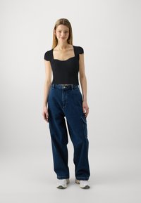 Črn rebrast kratek top z kvadratnim izrezom, ki je kombiniran z ohlapnimi temnimi denim cargo hlačami z bočnimi žepi in sproščenim krojem.