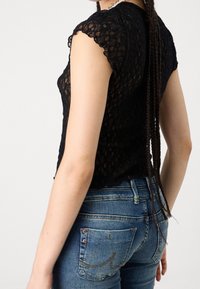 Top negro de encaje de manga corta con dobladillo con forma de ondas, combinado con jeans de mezclilla de lavado medio que tienen dos bolsillos traseros y costuras en contraste.