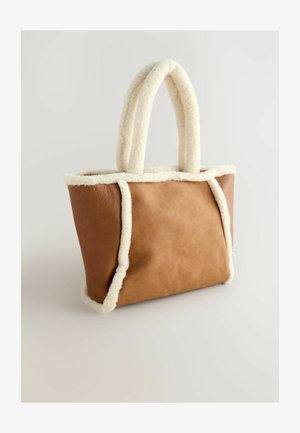 Bruine leren tote bag met crèmekleurige, donzige rand en handvatten. Heeft een minimalistisch ontwerp en een rechthoekige vorm.