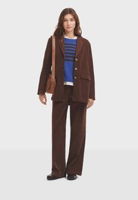 Blazer de pana marrón y pantalones a juego sobre un suéter de rayas azules. Bolso de cuero marrón, zapatos negros, textura suave en todo.