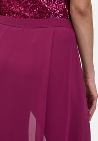 Robe fuchsia avec un corsage à sequins et une jupe fluide en chiffon, présentant un design plissé et une texture douce. Vue rapprochée de l'arrière.