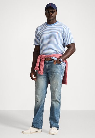 Īsa piedurkne, zila un balta svītraina T-krekle, izbalējuši zili džinsi, sarkans džemperis sasiets ap jostas, tumši zils cepure un baltas sporta botas.