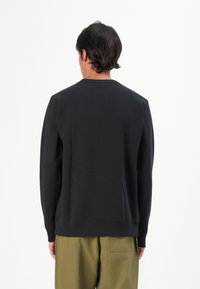 Felpa nera a girocollo con maniche lunghe, colletto e polsini a coste, tessuto testurizzato e orlo dritto. Indossata con pantaloni verde oliva.