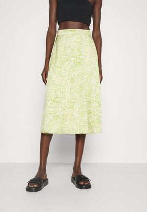 Woman wearing a light green patterned midi skirt, black crop top, and black slide sandals against a plain white background.
