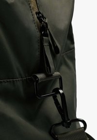 Bolsa de tela verde oscuro con superficie texturizada, con cremallera negra y herrajes, incluyendo un clip y una correa para un cierre seguro.