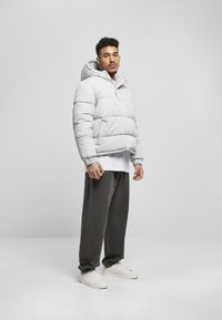 Hellgraue Daunenjacke mit Kapuze, mit gestepptem Design, elastischen Bündchen und lockerer Passform, kombiniert mit dunkelgrauen Hosen und weißen Sneakers.