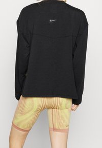 Camiseta negra de manga larga con logo en la parte de atrás combinada con pantalones cortos de ciclismo amarillos y rosas con un patrón de líneas texturizadas.