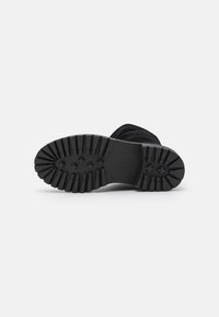 Suela de bota negra con un patrón de banda de rodadura resistente, que presenta ranuras profundas para tracción y un acabado limpio, fabricada con material de goma duradera.