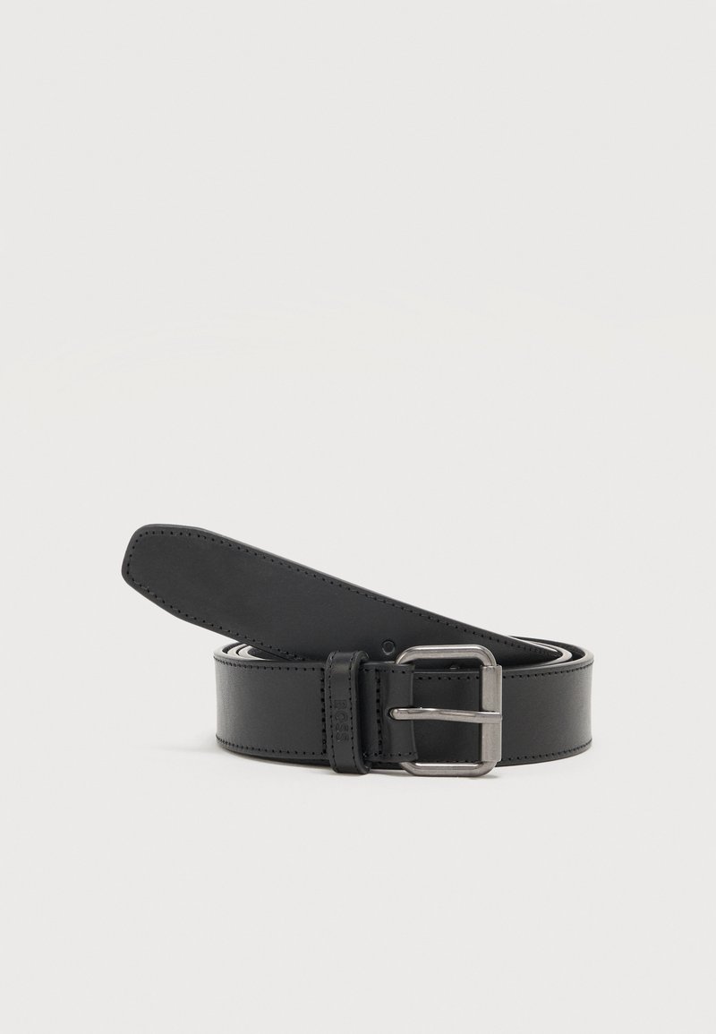 Ceinture en cuir noire enroulée avec une boucle rectangulaire en métal argenté sur un fond clair uni.